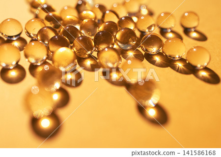 Close-up view of transparent water droplets scattered on a golden surface, reflecting light and creating a shimmering effect with soft shadows Close-up view of transparent water droplets scattered on a golden surface, reflecting light and creating a shimmering effect with soft shadows 141586168