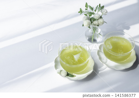 兩杯冰冷的綠茶沐浴在斑駁的陽光下,旁邊點綴著白色的金盞花——這是一幅令人神清氣爽的夏日款待的畫面。 兩杯冰冷的綠茶沐浴在斑駁的陽光下,旁邊點綴著白色的金盞花——這是一幅令人神清氣爽的夏日款待的畫面。 141586377