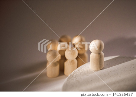 Wooden figurines of diverse shapes and sizes arranged in a group with one figure standing apart on a light surface, showcasing contrast and individuality in design 141586457