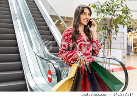 Pretty young woman in red striped shirt talking on the phone and looking contented Pretty young woman in red striped shirt talking on the phone and looking contented 141587114