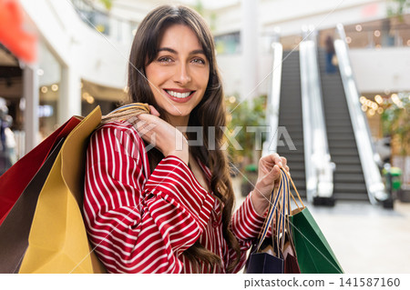Joyful caucasian young woman in red shirt with paper shopping bags Joyful caucasian young woman in red shirt with paper shopping bags 141587160