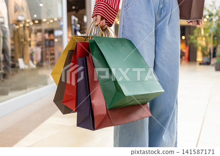 Close up of a woman walking in a shopping center with paper bags in hands Close up of a woman walking in a shopping center with paper bags in hands 141587171