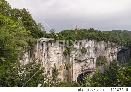 Towering vertical rock walls etched by time, plunging dramatically into a hidden valley where ancient caverns breach the cliffside. Towering vertical rock walls etched by time, plunging dramatically into a hidden valley where ancient caverns breach the cliffside. 141587546