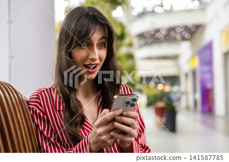 Cute young woman texting on the phone and looking excited Cute young woman texting on the phone and looking excited 141587785