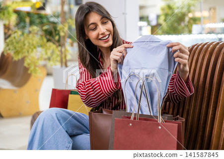Young woman looking at her new clothes after shopping and feeling contented Young woman looking at her new clothes after shopping and feeling contented 141587845