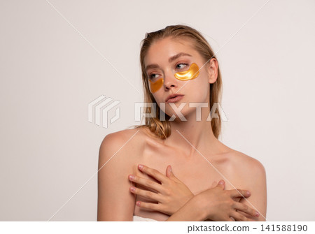 Woman wearing under eye patches, applying anti-aging facial product for skin treatment and beauty routine Woman wearing under eye patches, applying anti-aging facial product for skin treatment and beauty routine 141588190