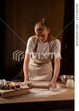 Woman baking fresh bread or pastry dough on rustic wooden kitchen table, rolling it with pin, creating artisan food Woman baking fresh bread or pastry dough on rustic wooden kitchen table, rolling it with pin, creating artisan food 141588204