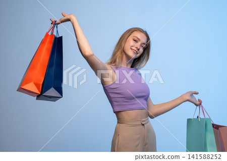 Happy young woman enjoying retail therapy, holding colorful shopping bags and smiling, feeling satisfaction from purchase Happy young woman enjoying retail therapy, holding colorful shopping bags and smiling, feeling satisfaction from purchase 141588252