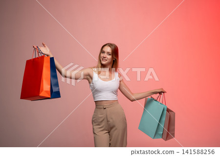 Smiling young woman holding colorful shopping bags expressing happiness and retail consumerism on sale Smiling young woman holding colorful shopping bags expressing happiness and retail consumerism on sale 141588256