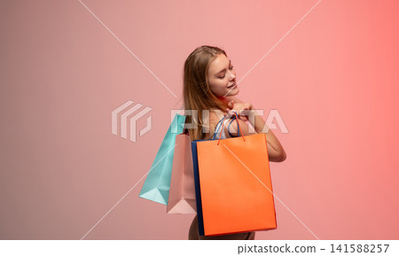 Happy young woman carrying colorful shopping bags after successful purchase on pink background Happy young woman carrying colorful shopping bags after successful purchase on pink background 141588257