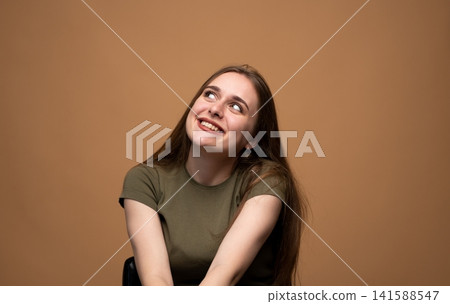 Young woman smiling, dreaming, and imagining, looking up with curiosity, posing in a studio Young woman smiling, dreaming, and imagining, looking up with curiosity, posing in a studio 141588547