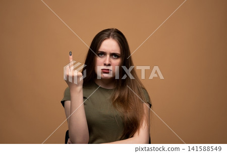 Young woman showing an obscene gesture, feeling angry, annoyed, and frustrated against a brown studio background Young woman showing an obscene gesture, feeling angry, annoyed, and frustrated against a brown studio background 141588549