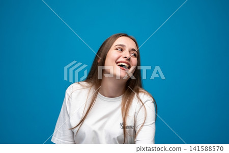 Young woman freely expressing joy and happiness, laughing a lot against a vibrant blue studio background Young woman freely expressing joy and happiness, laughing a lot against a vibrant blue studio background 141588570