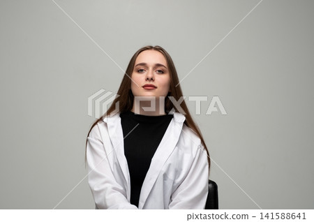 Young woman confidently posing in studio portrait, looking directly at camera with neutral expression Young woman confidently posing in studio portrait, looking directly at camera with neutral expression 141588641