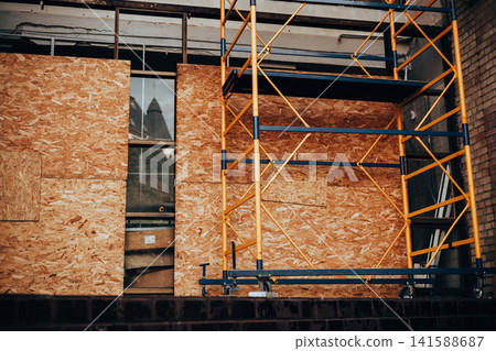 Construction scaffolding surrounding a modern building under renovation. Architectural facade with plywood panels illustrating urban development. Construction scaffolding surrounding a modern building under renovation. Architectural facade with plywood panels illustrating urban development. 141588687