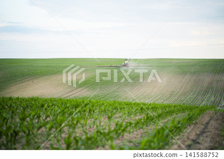 Farming equipment spraying crops in a green agricultural field, applying pesticides for crop health and yield Farming equipment spraying crops in a green agricultural field, applying pesticides for crop health and yield 141588752
