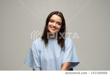 Young woman smiling, looking at camera, expressing joy and positivity in casual studio portrait Young woman smiling, looking at camera, expressing joy and positivity in casual studio portrait 141588988
