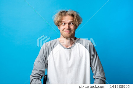 Young man creating a funny face and an awkward expression, looking away with side eye, showing suspiciousness and uncertainty on a vibrant blue background Young man creating a funny face and an awkward expression, looking away with side eye, showing suspiciousness and uncertainty on a vibrant blue background 141588995