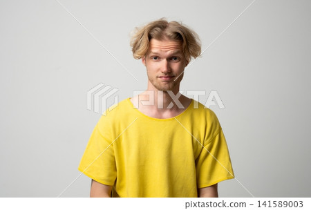 Young man showing skeptical expression with raised eyebrows and a slight smirk, questioning a situation or having doubts, wearing a casual yellow t-shirt on a gray background Young man showing skeptical expression with raised eyebrows and a slight smirk, questioning a situation or having doubts, wearing a casual yellow t-shirt on a gray background 141589003