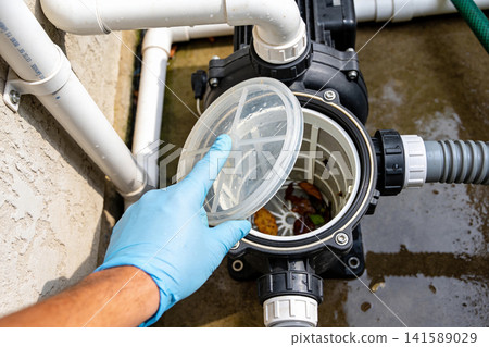 Hand in blue glove cleaning debris from pool pump filter basket Hand in blue glove cleaning debris from pool pump filter basket 141589029