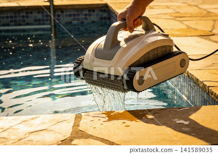 Hand holding robotic pool cleaner with water dripping into swimming pool Hand holding robotic pool cleaner with water dripping into swimming pool 141589035
