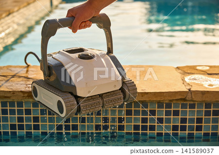Hand holding a robotic pool cleaner emerging from sparkling blue water Hand holding a robotic pool cleaner emerging from sparkling blue water 141589037