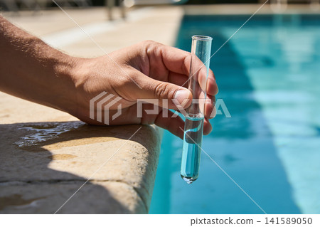 Hand holding test tube with blue liquid near swimming pool edge Hand holding test tube with blue liquid near swimming pool edge 141589050