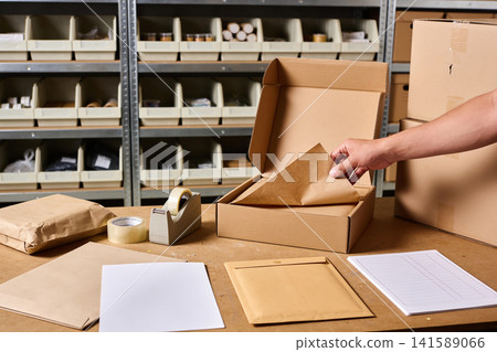 Hand packing a cardboard box with protective paper in a warehouse setting Hand packing a cardboard box with protective paper in a warehouse setting 141589066