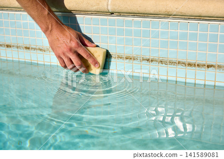 Hand cleaning pool tiles with a sponge to remove algae and grime Hand cleaning pool tiles with a sponge to remove algae and grime 141589081