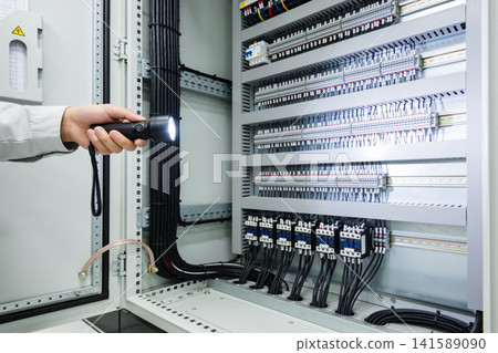 Electrician inspecting a complex electrical panel with a flashlight Electrician inspecting a complex electrical panel with a flashlight 141589090