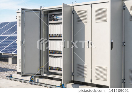 Outdoor electrical cabinet with open door showing internal components and solar panels 141589091