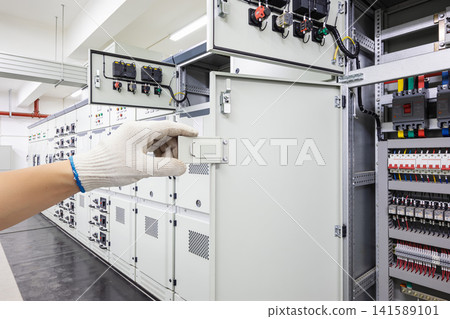 Electrician wearing gloves inspects a large electrical panel with many switches and wires Electrician wearing gloves inspects a large electrical panel with many switches and wires 141589101