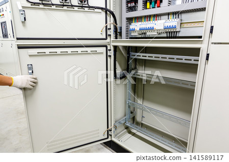Electrician's hand in glove opening a large industrial electrical control panel Electrician's hand in glove opening a large industrial electrical control panel 141589117