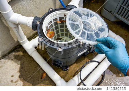 Pool pump basket cleaning: gloved hand removing debris from filter basket Pool pump basket cleaning: gloved hand removing debris from filter basket 141589215
