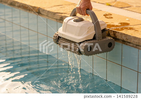 Person removing a robotic pool cleaner from the water, dripping water Person removing a robotic pool cleaner from the water, dripping water 141589228