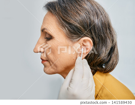 ENT doctor cleans patient's ear with cotton stick, remove earwax at medical clinic, side view ENT doctor cleans patient's ear with cotton stick, remove earwax at medical clinic, side view 141589430