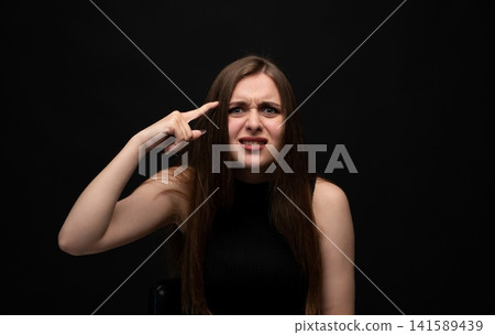 Frustrated young woman making crazy gesture with finger on temple, expressing irritation and confusion Frustrated young woman making crazy gesture with finger on temple, expressing irritation and confusion 141589439