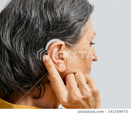 Hearing aid behind the ear of senior woman, close-up Hearing aid behind the ear of senior woman, close-up 141589473