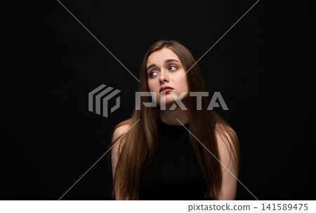 Young woman showing annoyance, boredom, and indifference with a sidelong glance on black background Young woman showing annoyance, boredom, and indifference with a sidelong glance on black background 141589475