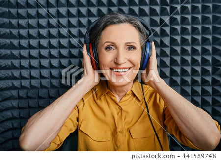 Hearing loss treatment. Positive mature woman wearing audiometry headphones while hearing test and audiogram in special audio room Hearing loss treatment. Positive mature woman wearing audiometry headphones while hearing test and audiogram in special audio room 141589748