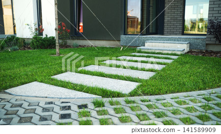 Contemporary house garden showcasing a path of rectangular stone slabs on vibrant green grass leading to the entrance steps 141589909