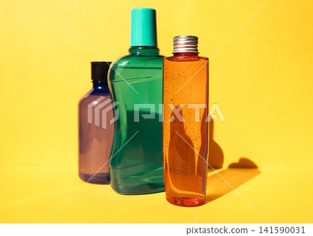 Three colorful plastic bottles in varying shapes and sizes, featuring a green bottle with a cap, a purple bottle, and an orange bottle against a bright yellow background Three colorful plastic bottles in varying shapes and sizes, featuring a green bottle with a cap, a purple bottle, and an orange bottle against a bright yellow background 141590031