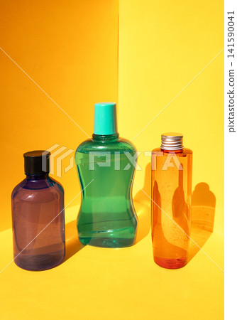 Three colorful plastic bottles in varying shapes and sizes, featuring a purple, green, and orange design against a bright yellow background Three colorful plastic bottles in varying shapes and sizes, featuring a purple, green, and orange design against a bright yellow background 141590041
