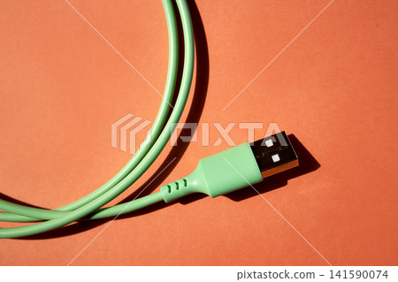 Green USB cable with a rectangular connector lying on an orange background, showcasing the cable's texture and design details for technology-related content Green USB cable with a rectangular connector lying on an orange background, showcasing the cable's texture and design details for technology-related content 141590074