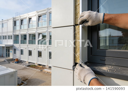 Construction worker installing modern modular building facade panels and insulation Construction worker installing modern modular building facade panels and insulation 141590093