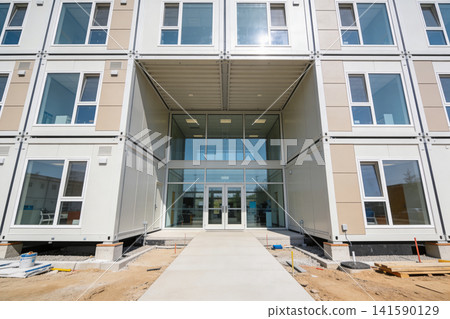 Modern modular building entrance with stacked shipping container units and large glass facade Modern modular building entrance with stacked shipping container units and large glass facade 141590129