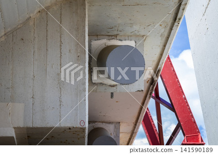 Close-up view of concrete bridge structure with red steel beams and blue sky 141590189