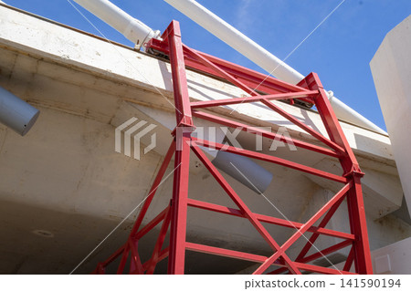 Red scaffolding under a concrete bridge with blue sky backdrop Red scaffolding under a concrete bridge with blue sky backdrop 141590194