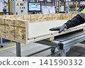 Worker assembling a custom wooden crate on a factory conveyor belt 141590332