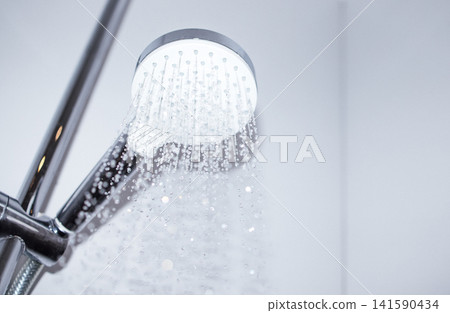 Modern chrome showerhead with water droplets cascading down, mounted on a sleek wall in a contemporary bathroom setting, emphasizing cleanliness and design Modern chrome showerhead with water droplets cascading down, mounted on a sleek wall in a contemporary bathroom setting, emphasizing cleanliness and design 141590434